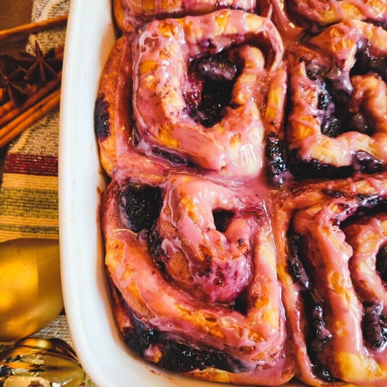 Baked cherry cinnamon roll with cherry glaze in a white baking pan.