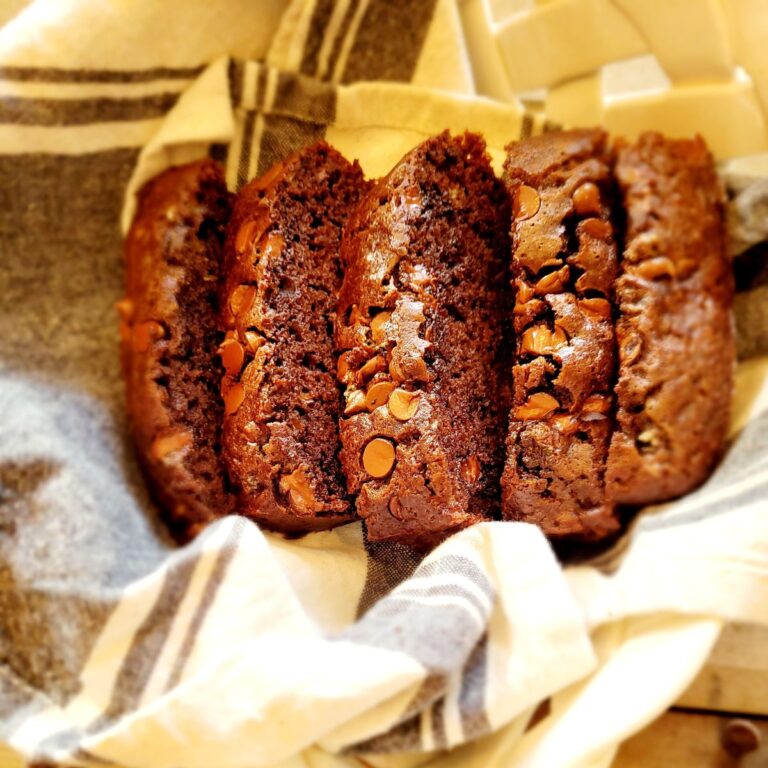 Chocolate banana bread with chocolate chips on top wrapped in a towel on top of a table.