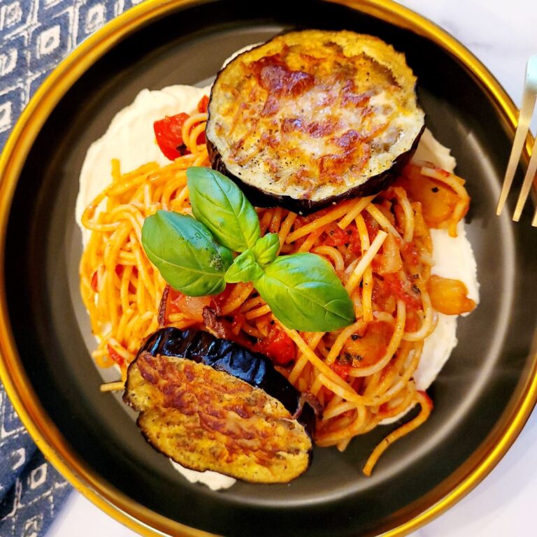 Spaghetti marinara on a bed of whipped ricotta with roast eggplant on top garnished with basil.