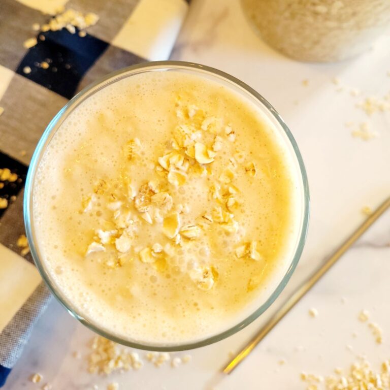 Smoothie in a glass on a counter top with oats on top, a straw, and a kitchen towel.