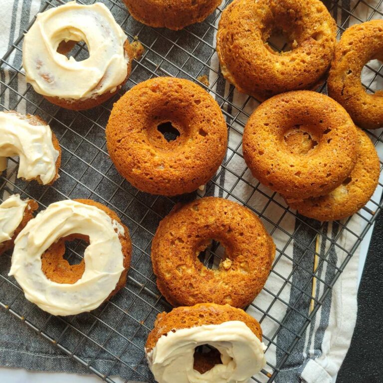 Multiple donuts that are either frosted, or not frosted, on a counter top and wire rack.
