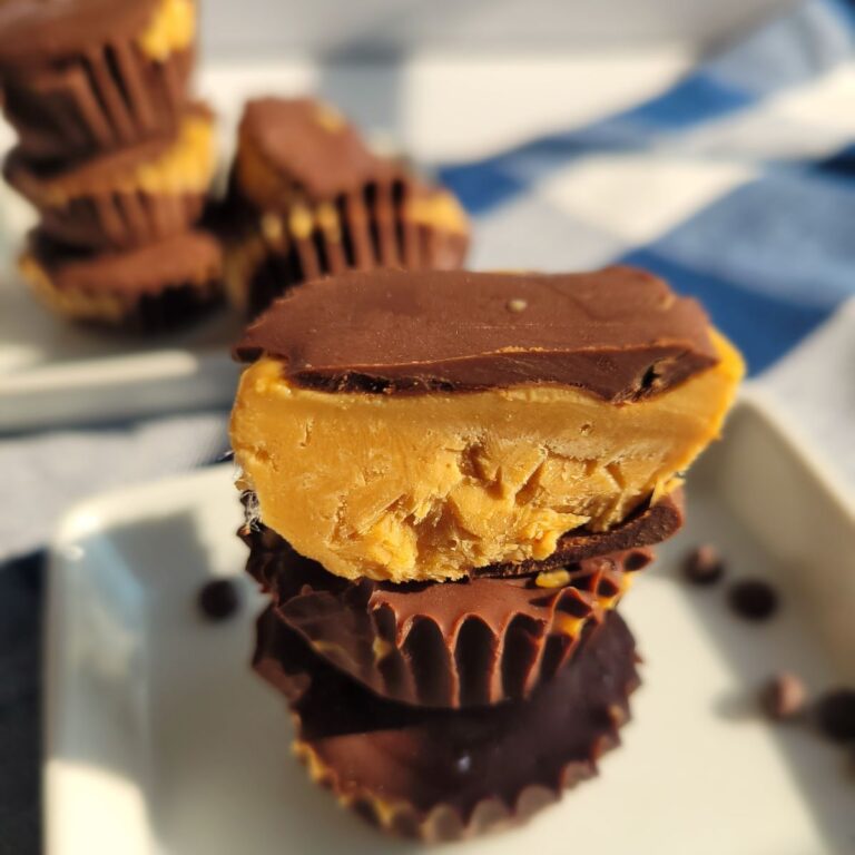 Peanut butter cups stacked on a white plate on a counter top with a blue kitchen towel.