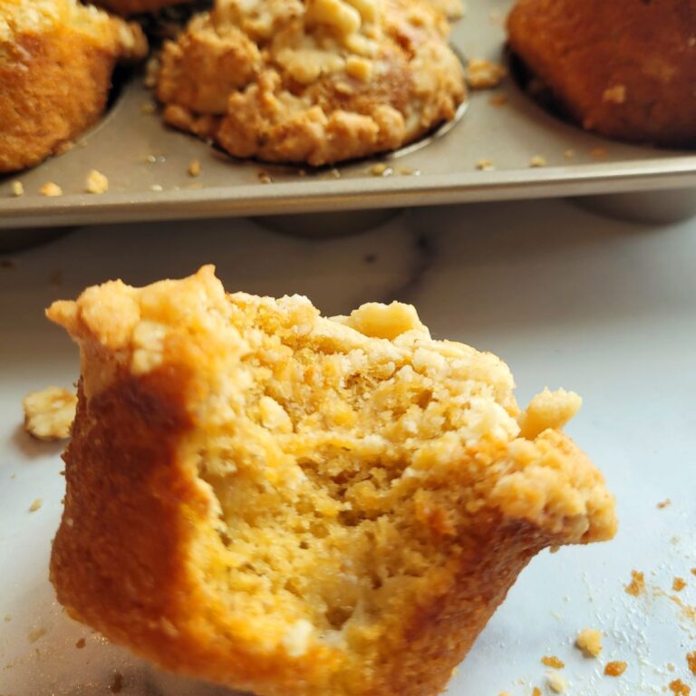 A pumpkin banana muffin on a counter top with other muffins in a cupcake pan in the background.