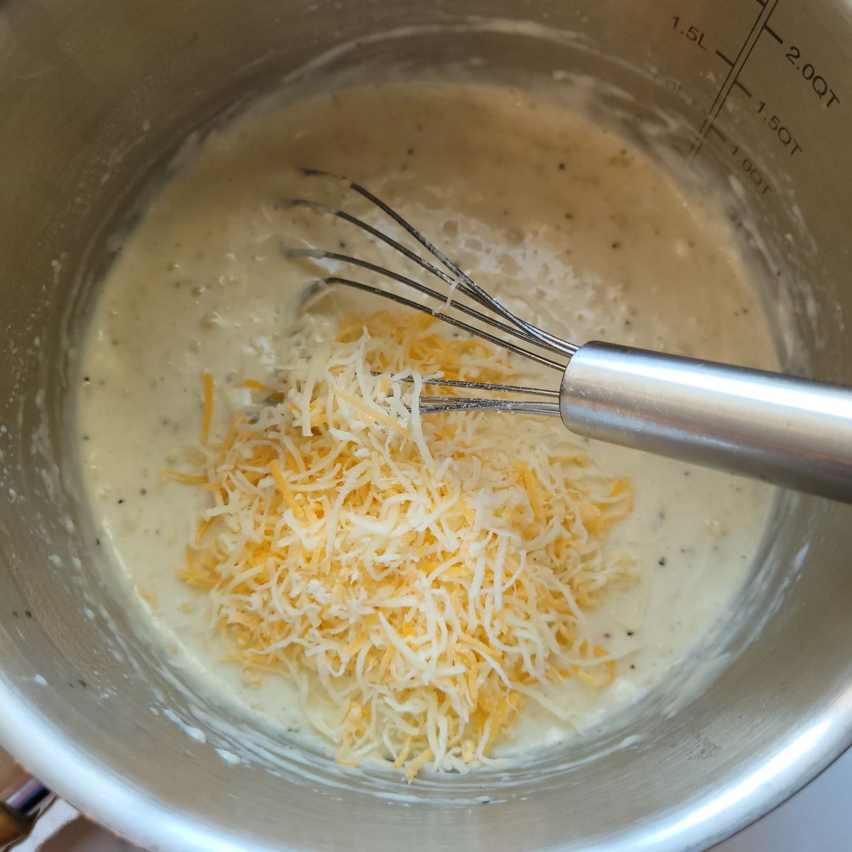 Adding cheese to milk mixture with a whisk in a saucepan.