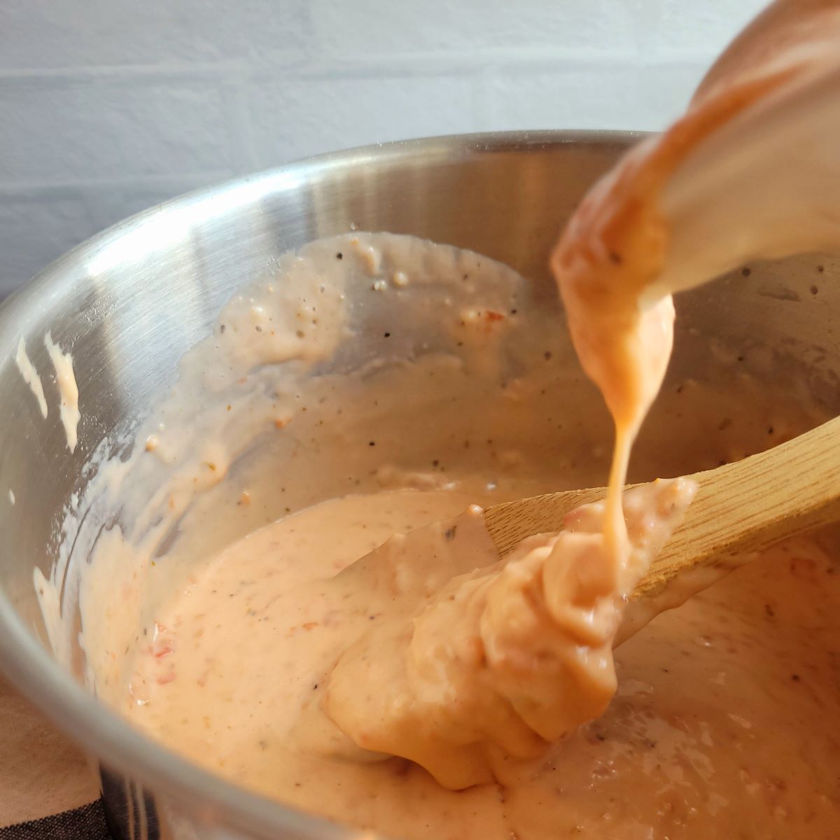 Homemade salsa with queso being poured into a medium saucepan onto a wooden spoon.