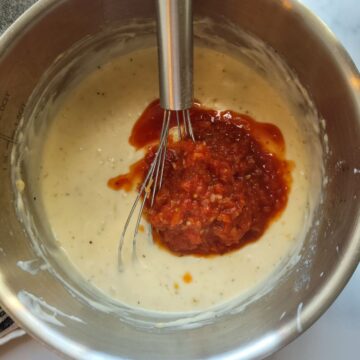 Adding salsa to homemade queso with a whisk in a saucepan.