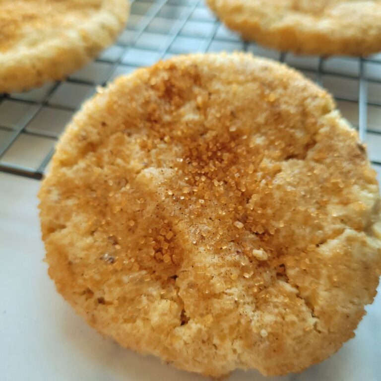 Baked snickerdoodle cookie on a cooling rack, surrounded by other cookies.