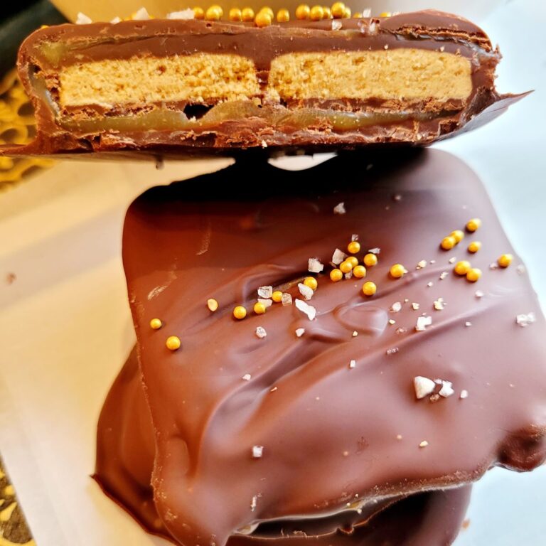Chocolate covered graham crackers with caramel that are cut in half on a piece of parchment paper.