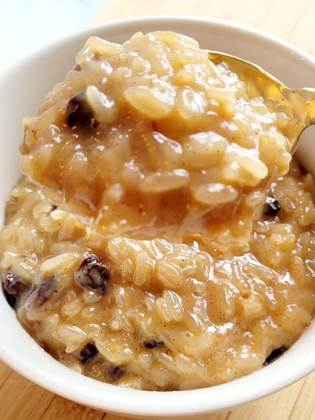 Rice pudding with raisins in a white bowl with a gold spoon.