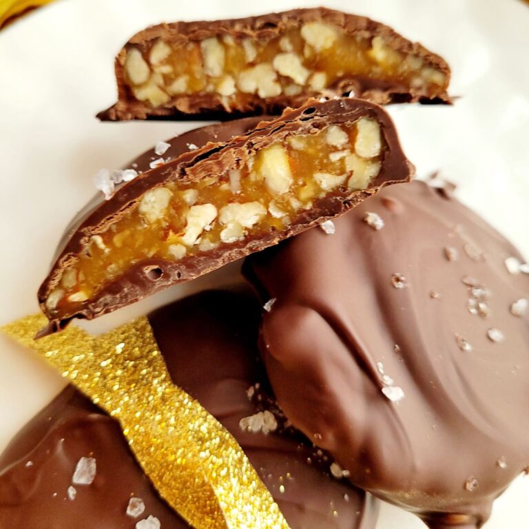 Pecan clusters that are coated in chocolate and wrapped in ribbon and presented on a white plate.