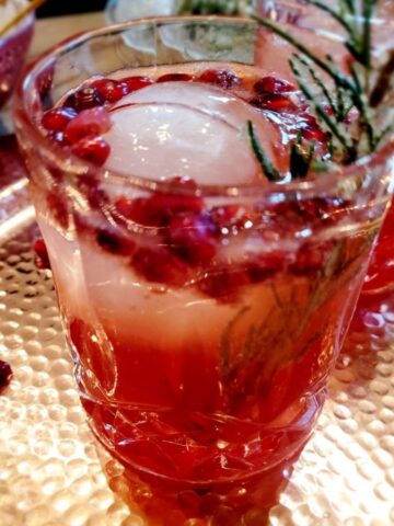 Pomegranate cocktail on a decorative tray that is garnished with sugared rosemary.