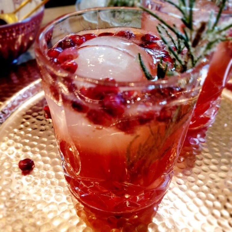 Pomegranate cocktail on a decorative tray that is garnished with sugared rosemary.