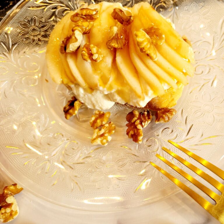 Ricotta toast with sliced pears, walnuts, and honey on a clear decorative plate with a gold fork.