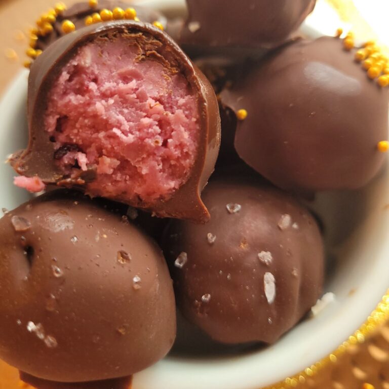 Raspberry chocolate truffles in a white decorative bowl with gold sprinkles.