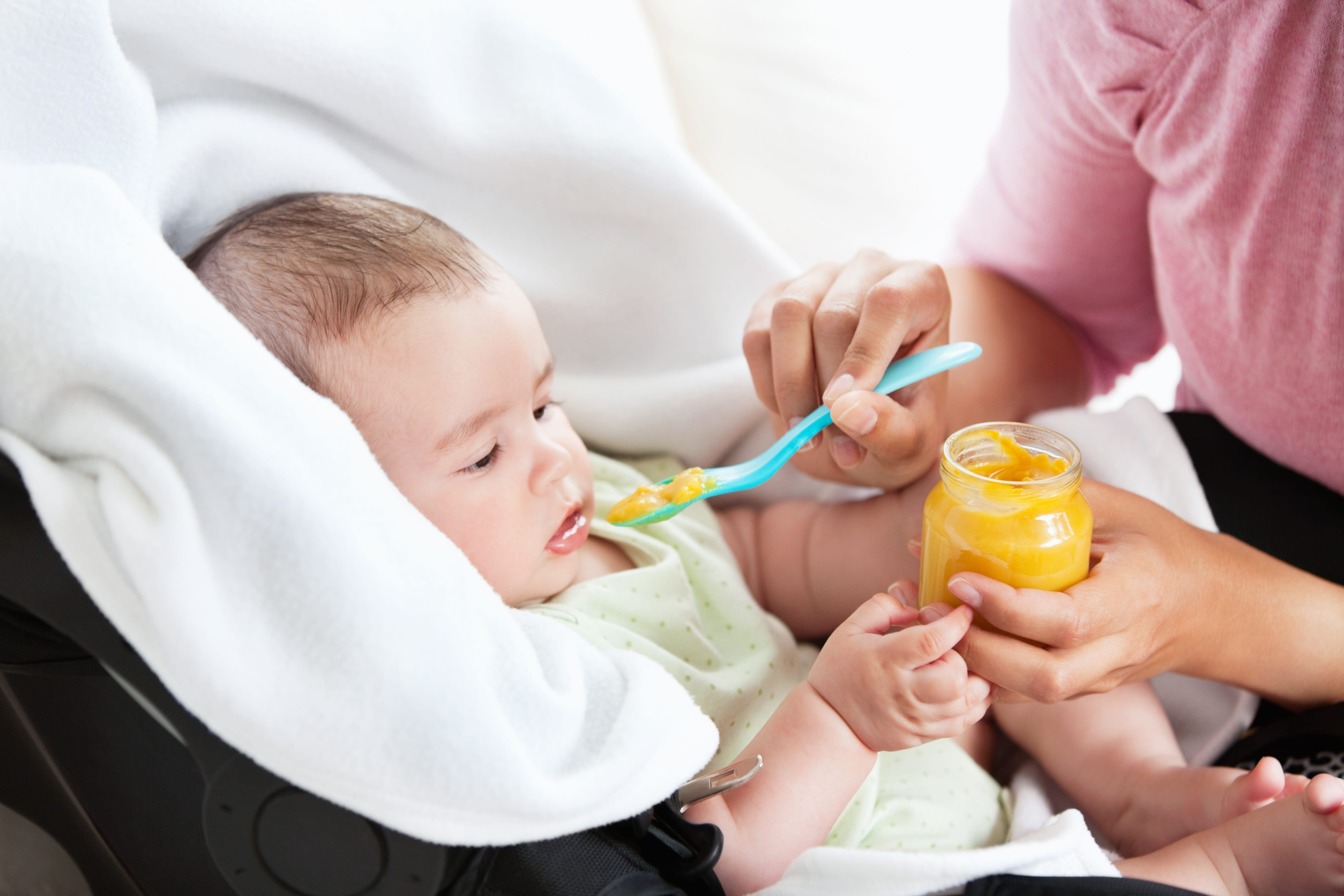 Close-up of a young mother giving carrot puree to her baby for lunch in the living-room