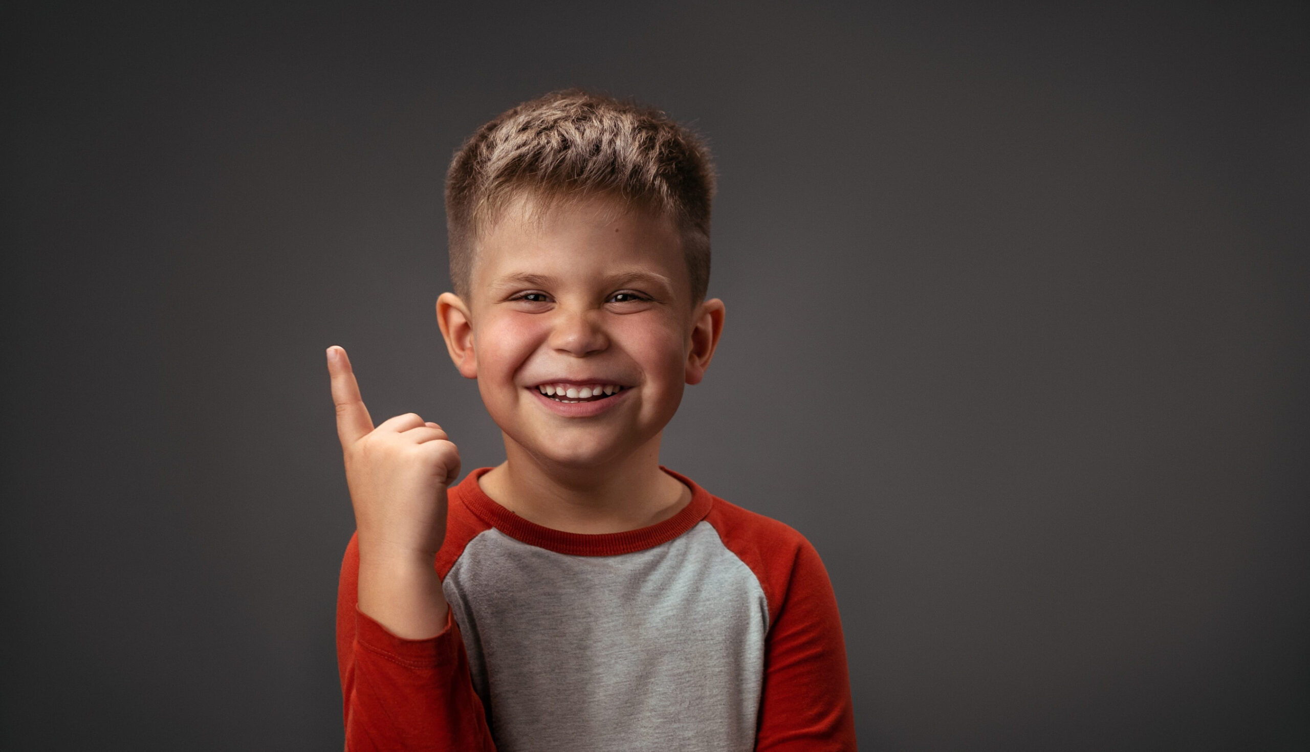 Charming boy points his finger up against an isolated background. Portrait of a smiling boy in the studio. High quality photo.