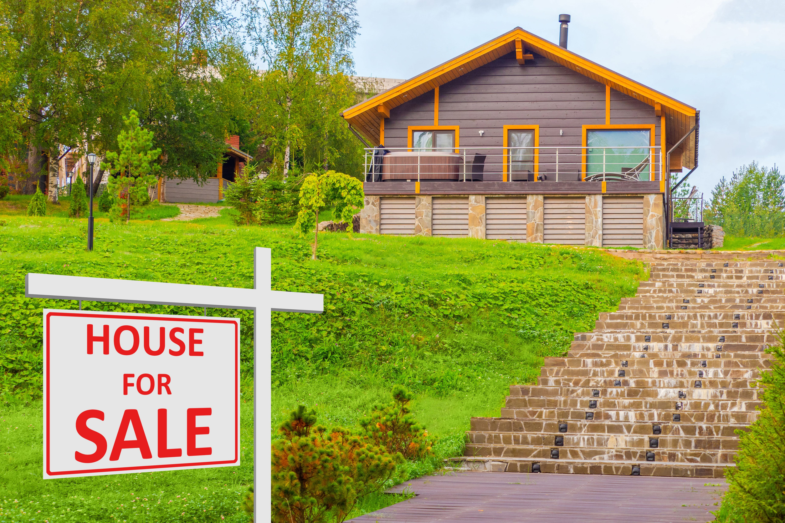 Announcement of sale stands near a private house. Hous for sale boar next to cottage. Country house is up for sale. Country cottage in background. Concept - searching for a house to buy.