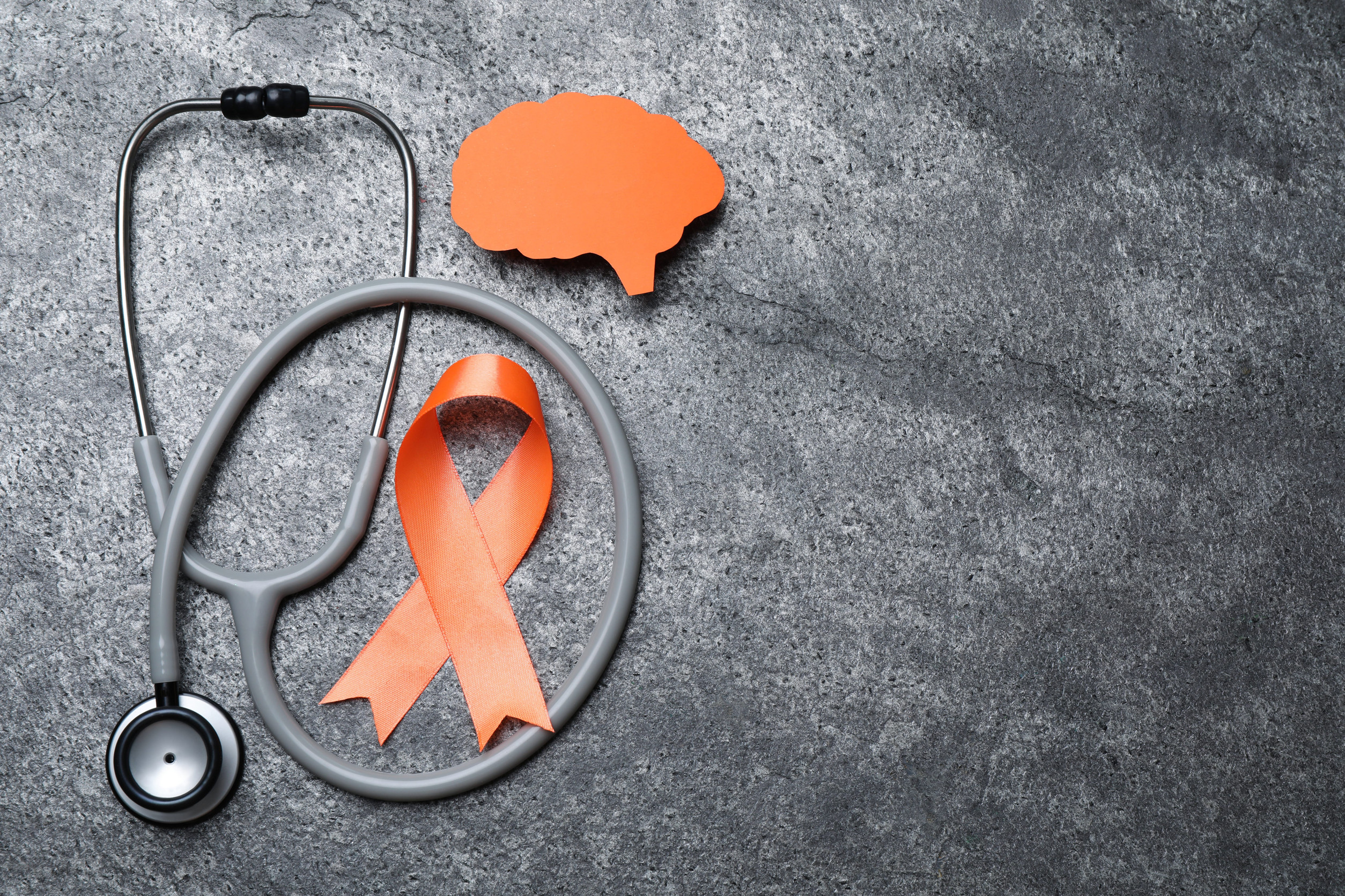 Orange ribbon, stethoscope and paper brain cutout on gray table, flat lay with space for text. Multiple sclerosis awareness