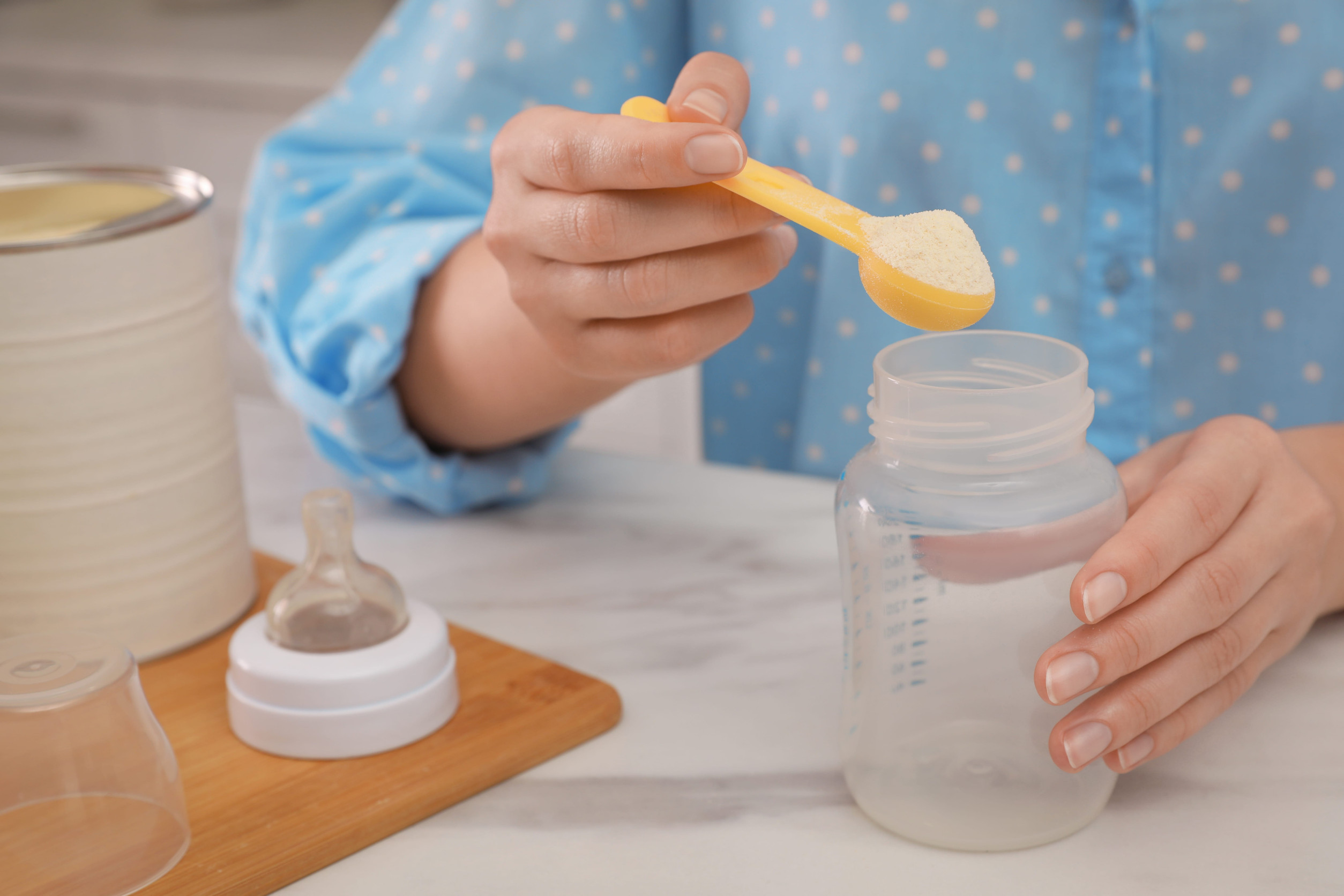 Woman preparing infant formula at table indoors, closeup. Baby milk
