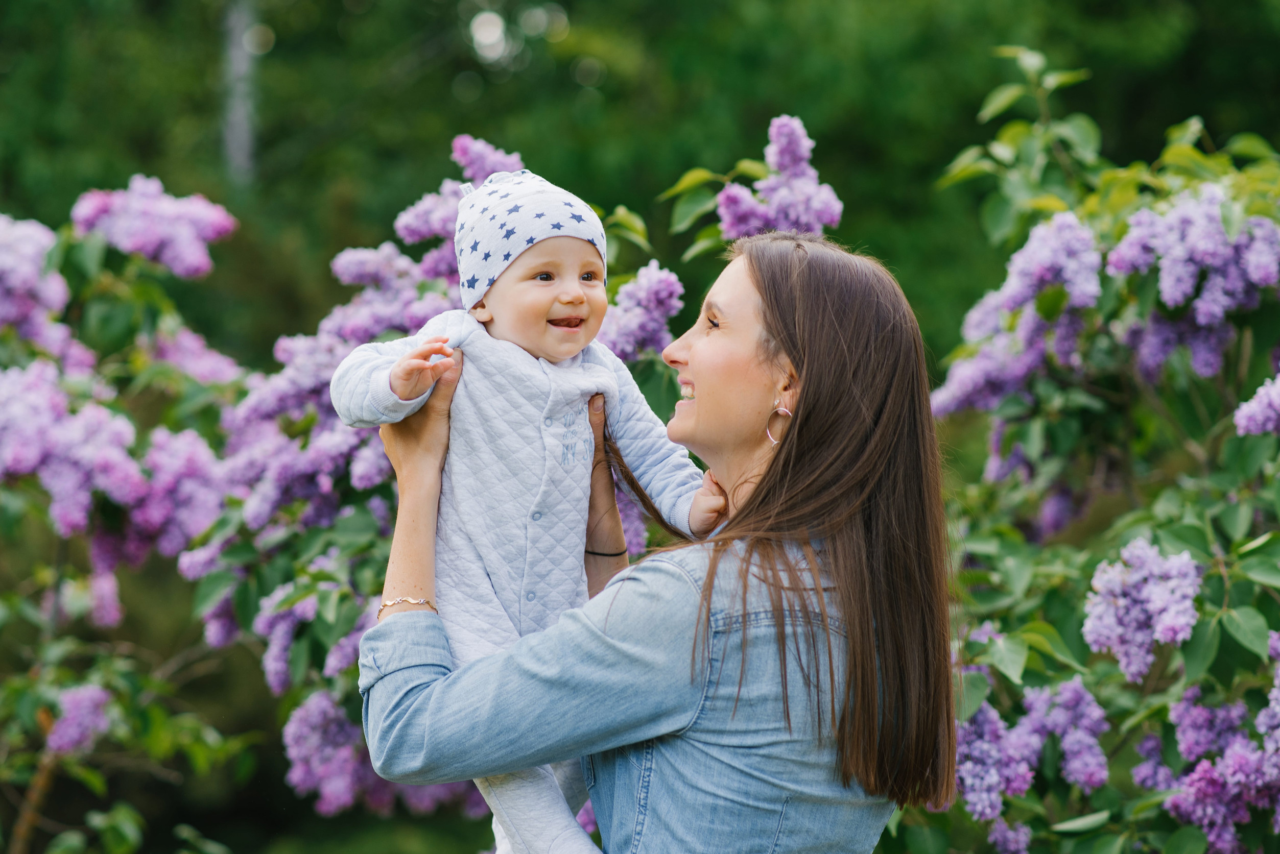 Happy European mother lifts up her little smiling son in her arms in the spring on a walk in the park