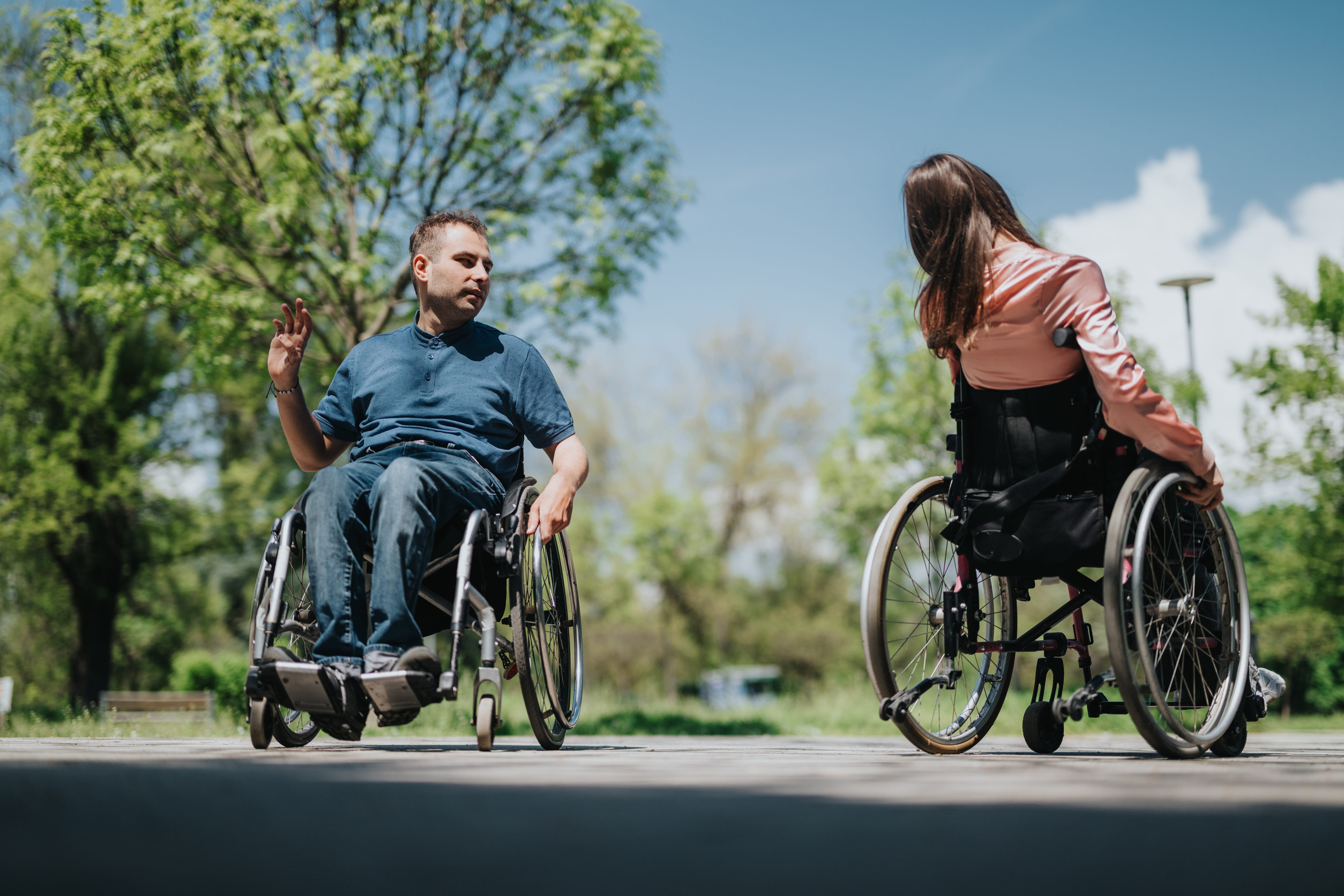Two individuals in wheelchairs enjoying a sunny day outdoors in a park setting