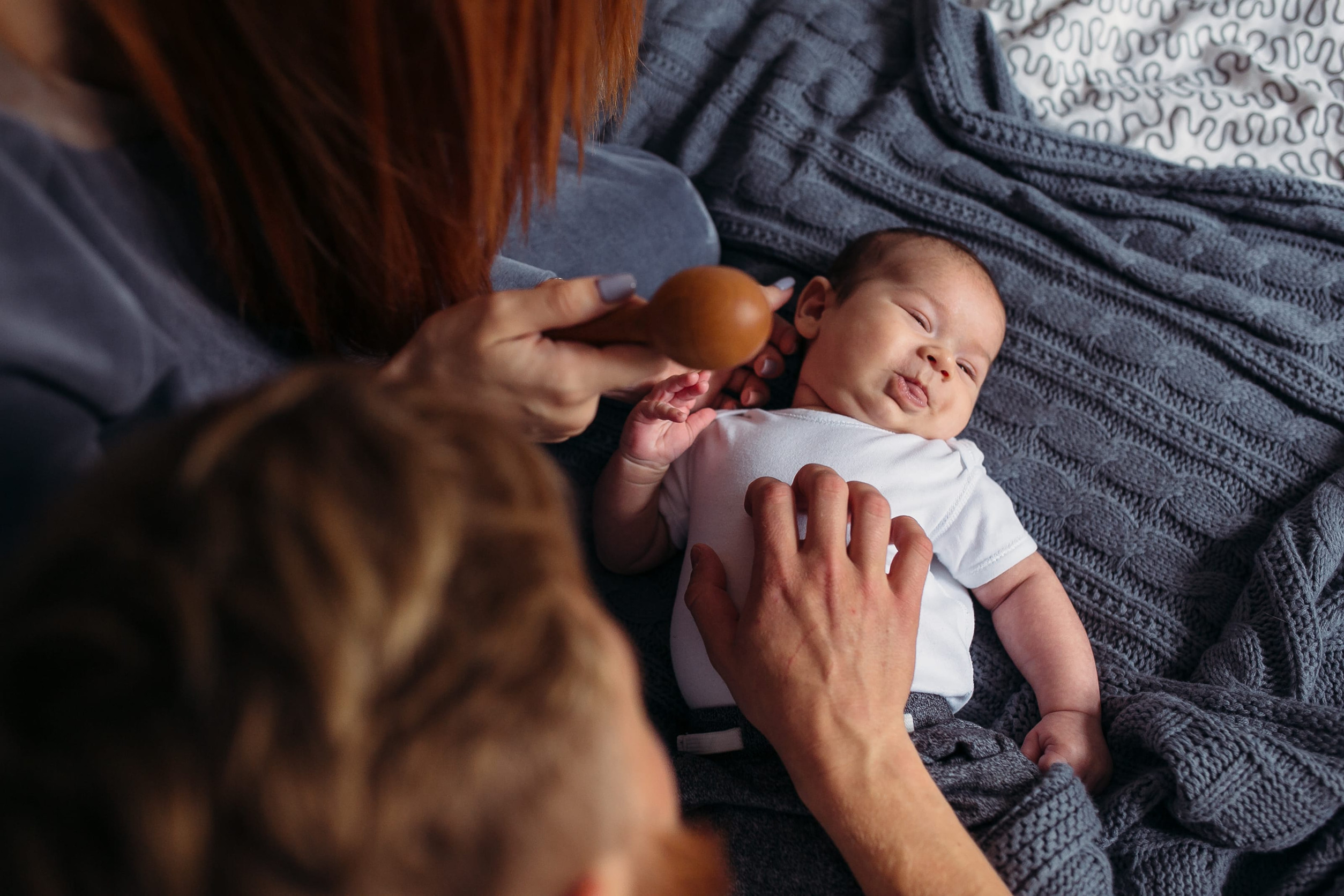 Young parents giving lots of attention to their baby. They are all sitting on a bed at home.