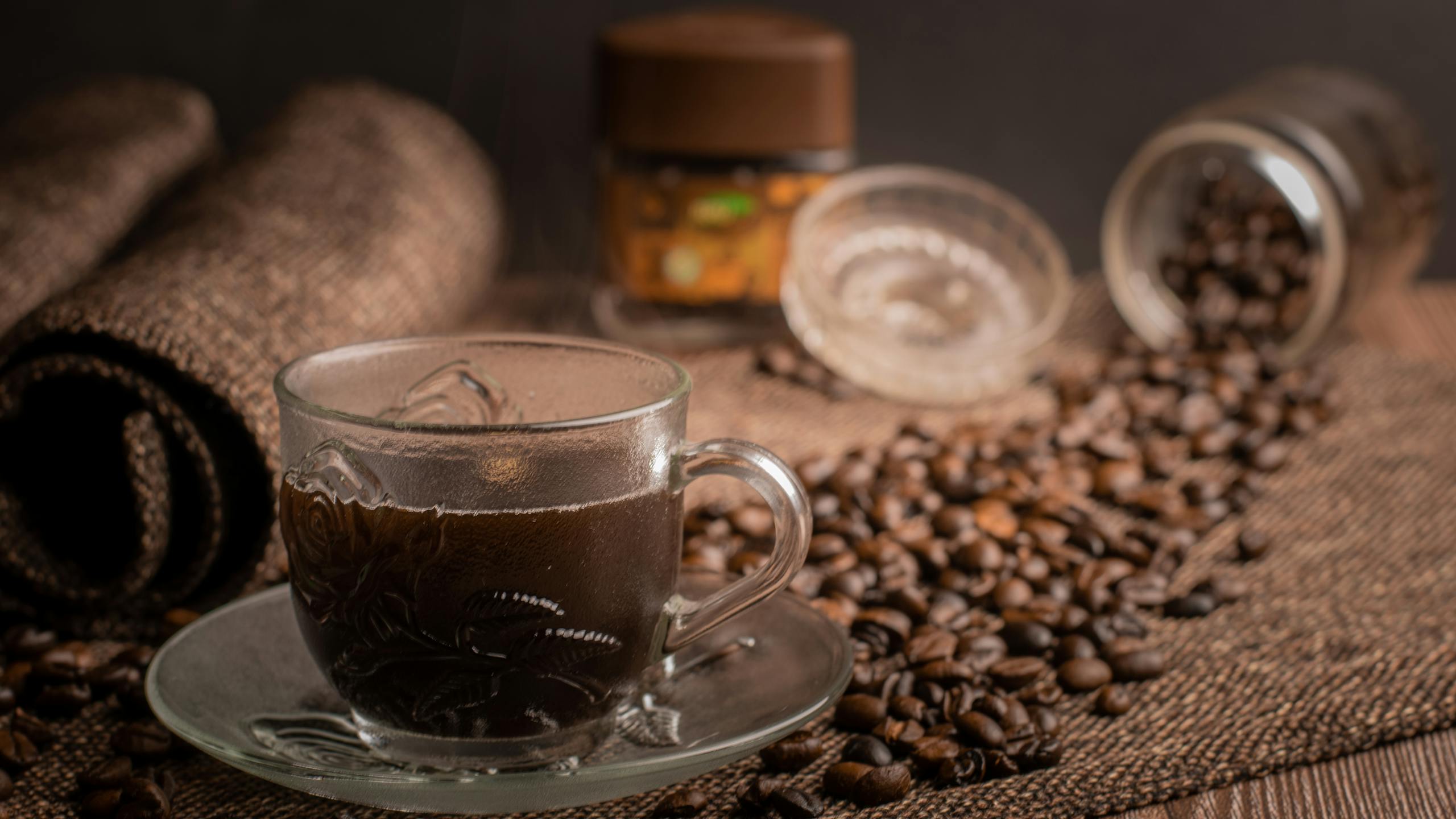 A beautifully styled espresso in a glass cup surrounded by scattered coffee beans, creating a warm, inviting atmosphere.