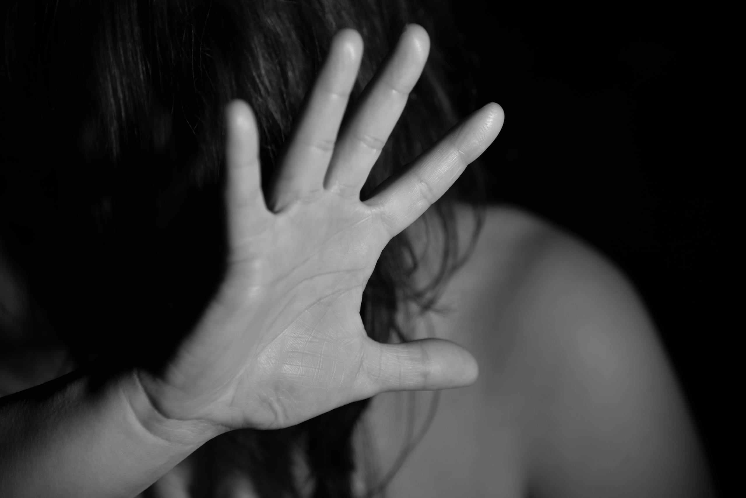 A black and white photo of a woman raising her hand, obscuring her face, suggesting a stop gesture.