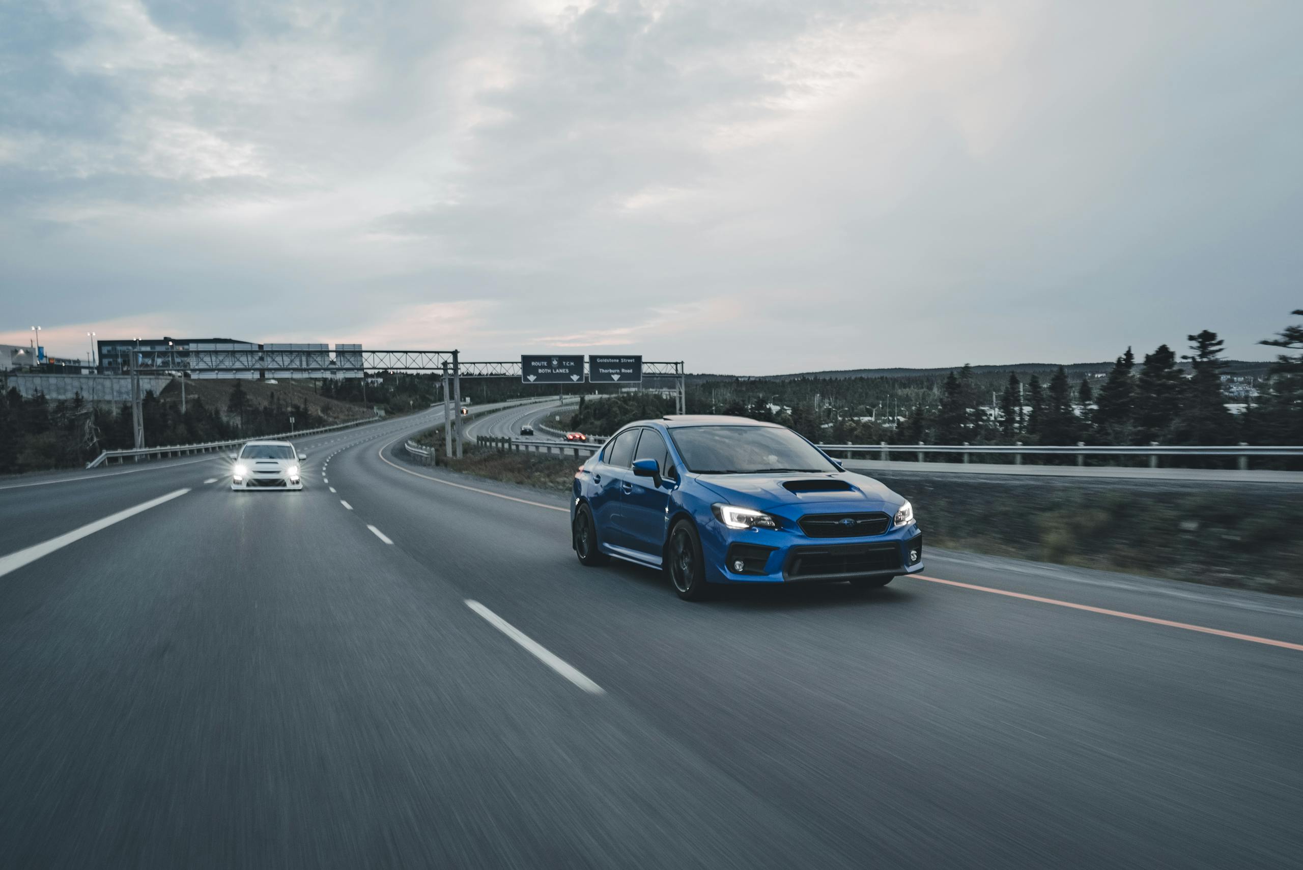 A blue Subaru WRX drives on an empty highway during dusk, showcasing speed and performance.