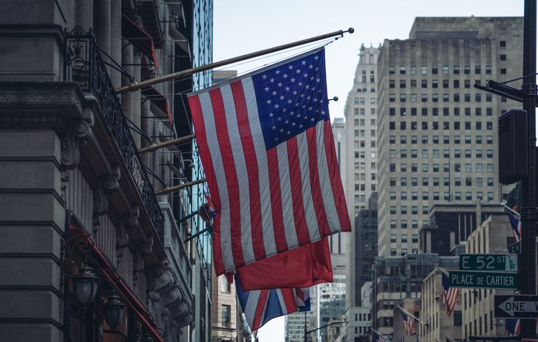 A bustling urban street in New York City with the American flag waving prominently among skyscrapers.