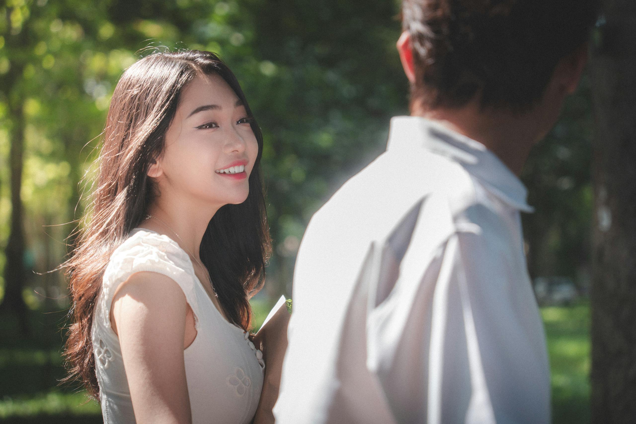 A candid moment of a young couple smiling in a sunlit park setting.