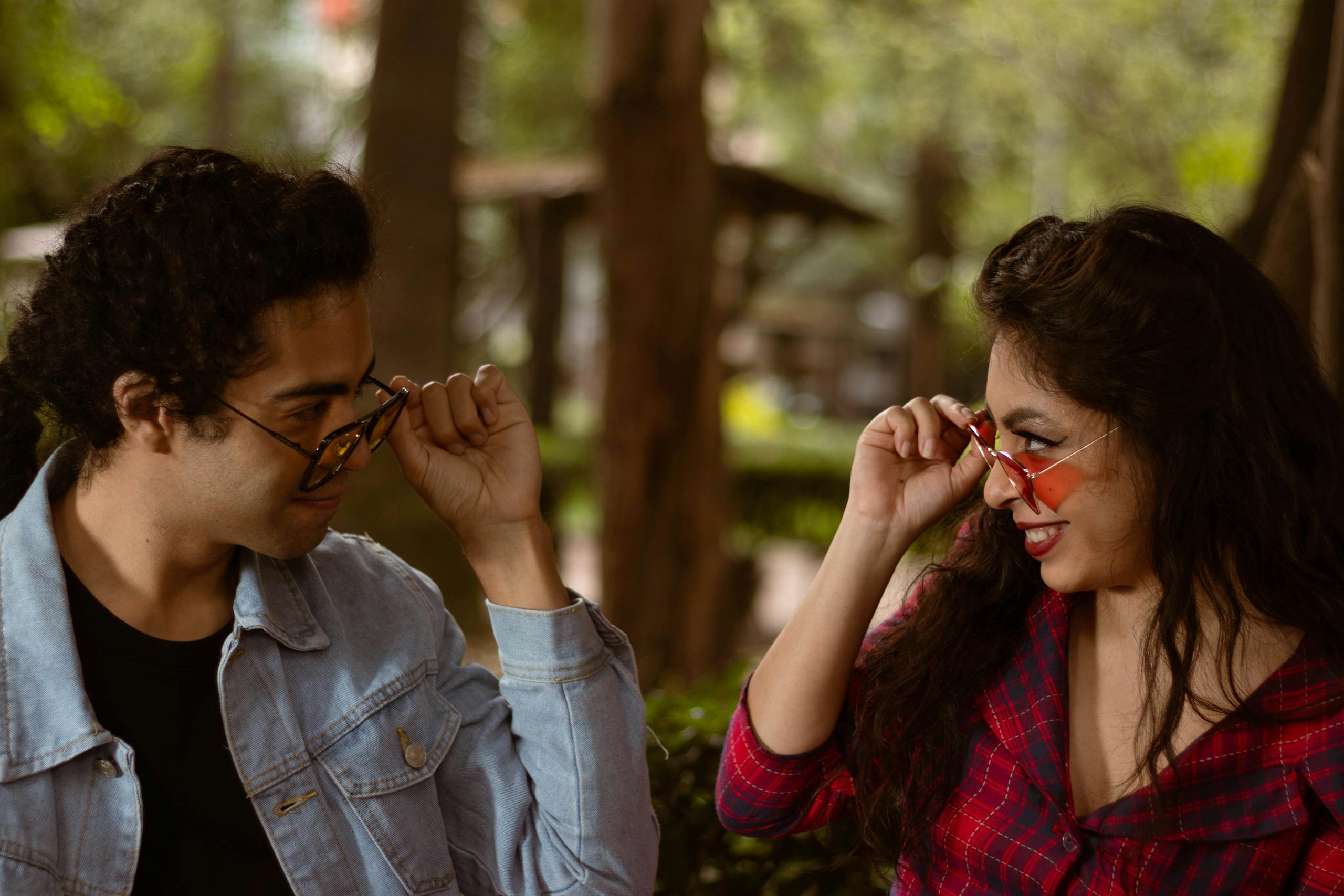 A cheerful couple enjoys a playful moment outdoors adjusting their sunglasses.