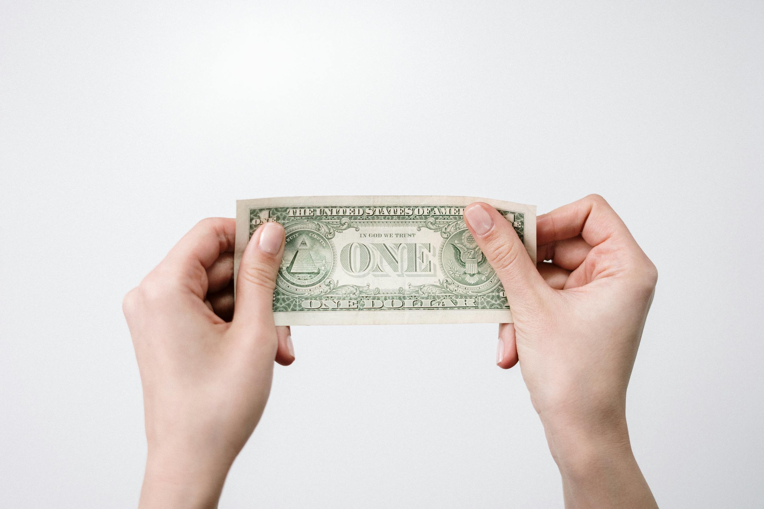 A close-up image of hands holding a one dollar bill, symbolizing finance and economy.