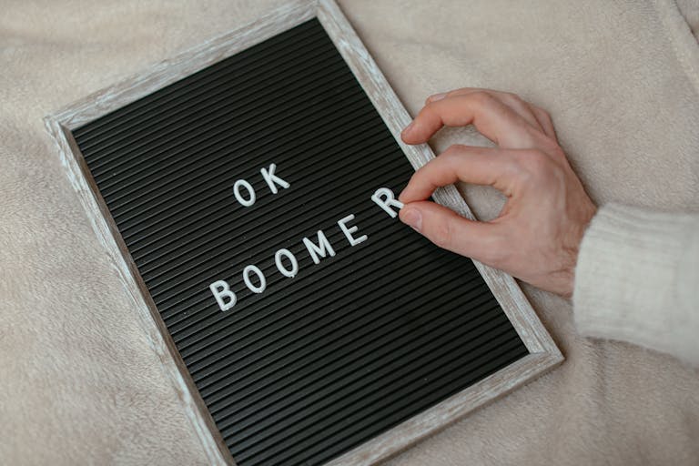 A close-up of a hand arranging letters to spell 'OK Boomer' on a felt letter board.