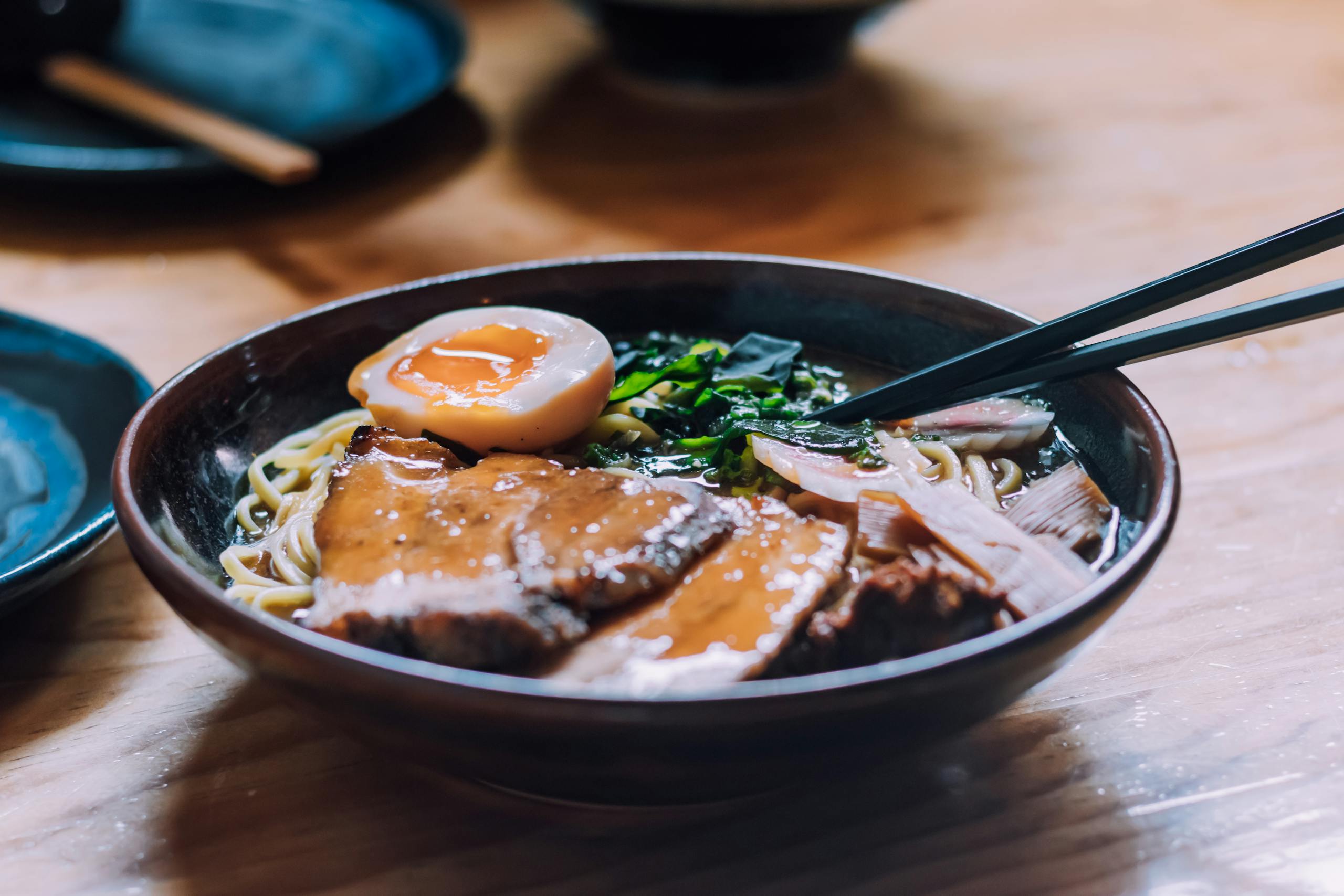 A close-up of a savory ramen bowl with pork, egg, and chopsticks on a wooden table.