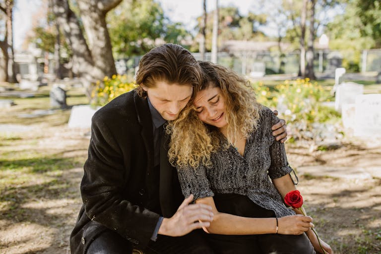 A comforting embrace in a serene graveyard captures grief and support.