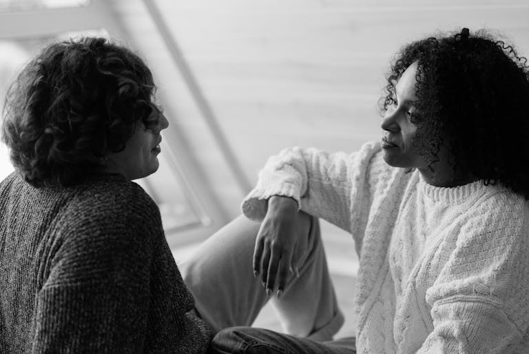 A couple in knitted sweaters sits face to face, engaging in a heartfelt conversation indoors.