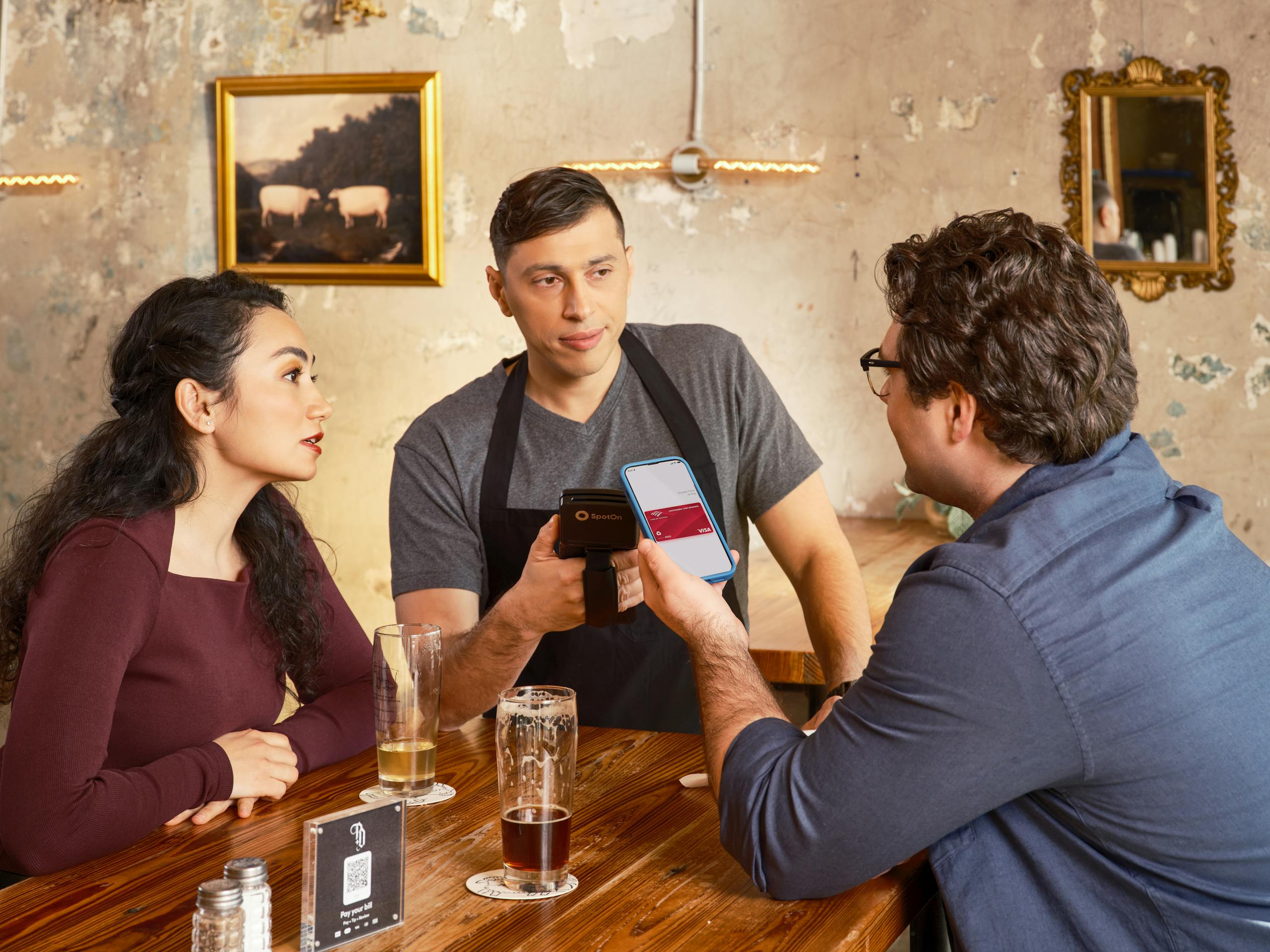 A couple makes a contactless payment using a smartphone at a restaurant bar counter.