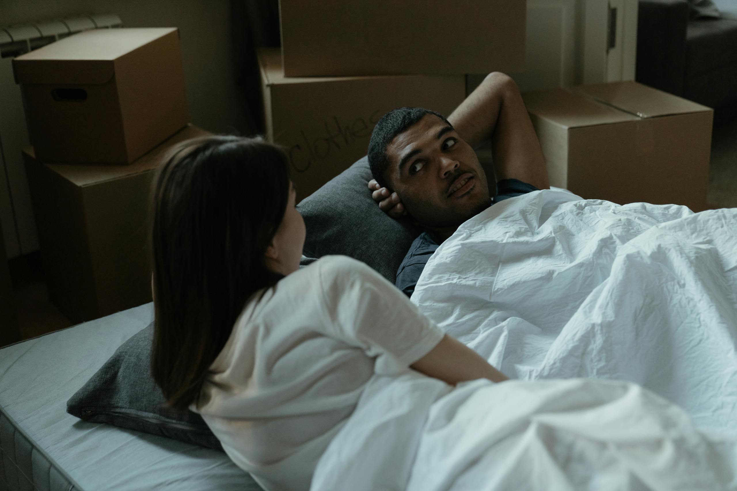 A couple relaxing in bed surrounded by cardboard boxes, indicating a recent move.