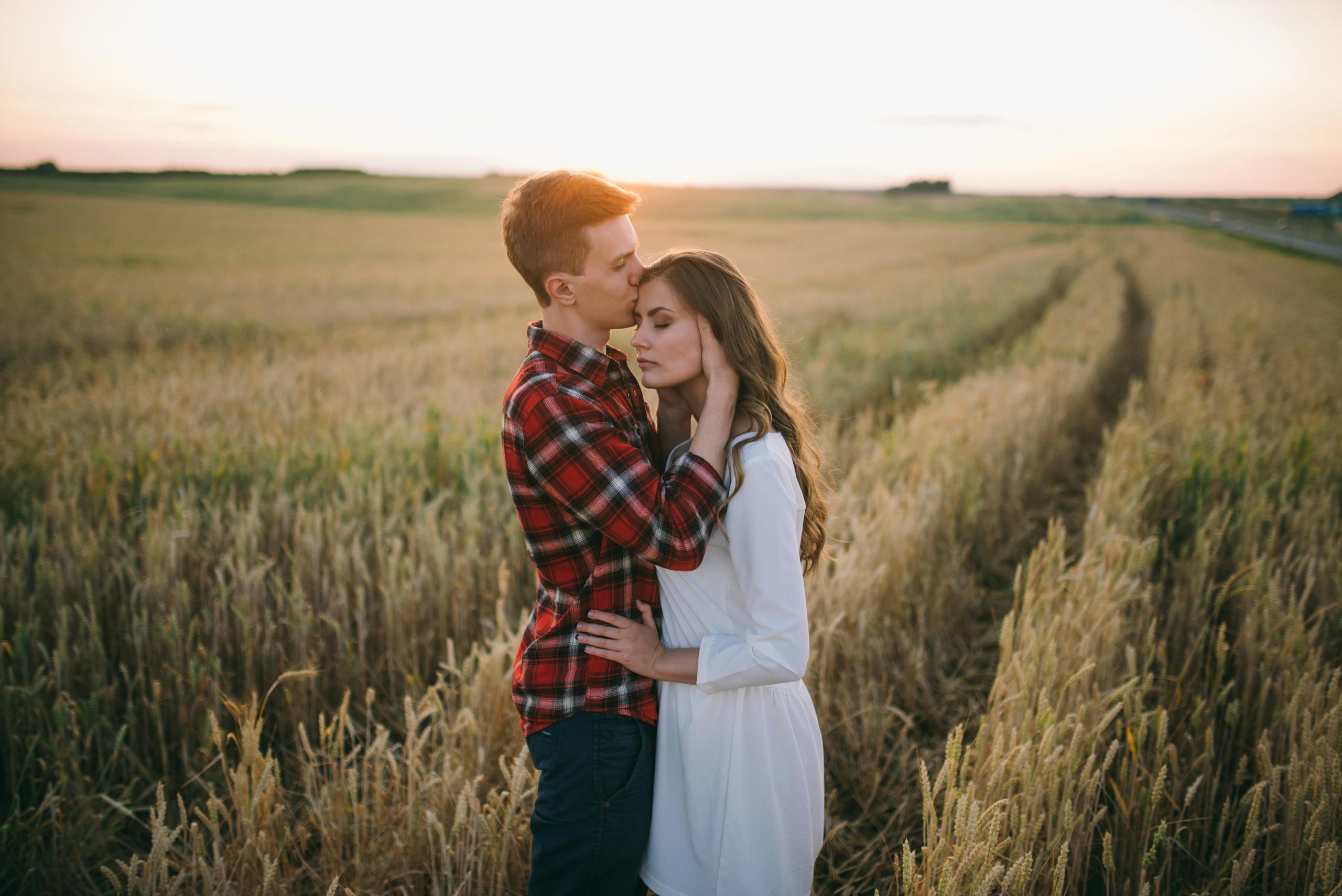A couple shares a tender moment in a rural wheat field during sunset, capturing romance and tranquility.