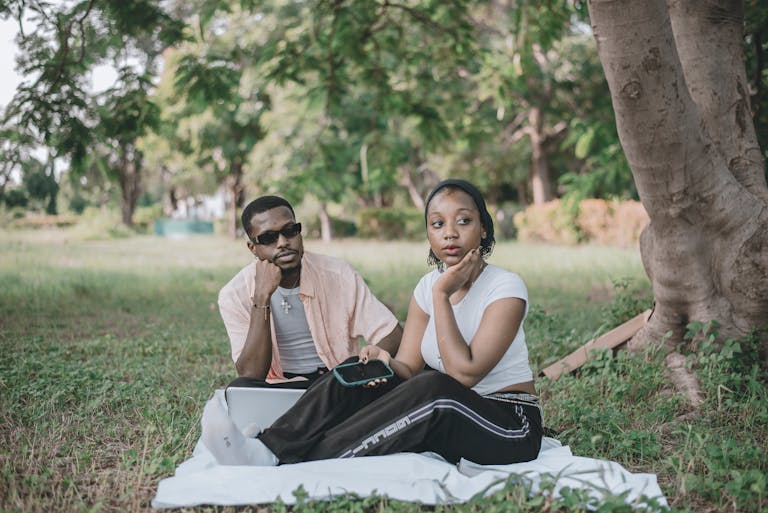 A couple sits together on a blanket in a lush park, enjoying leisure time outdoors.