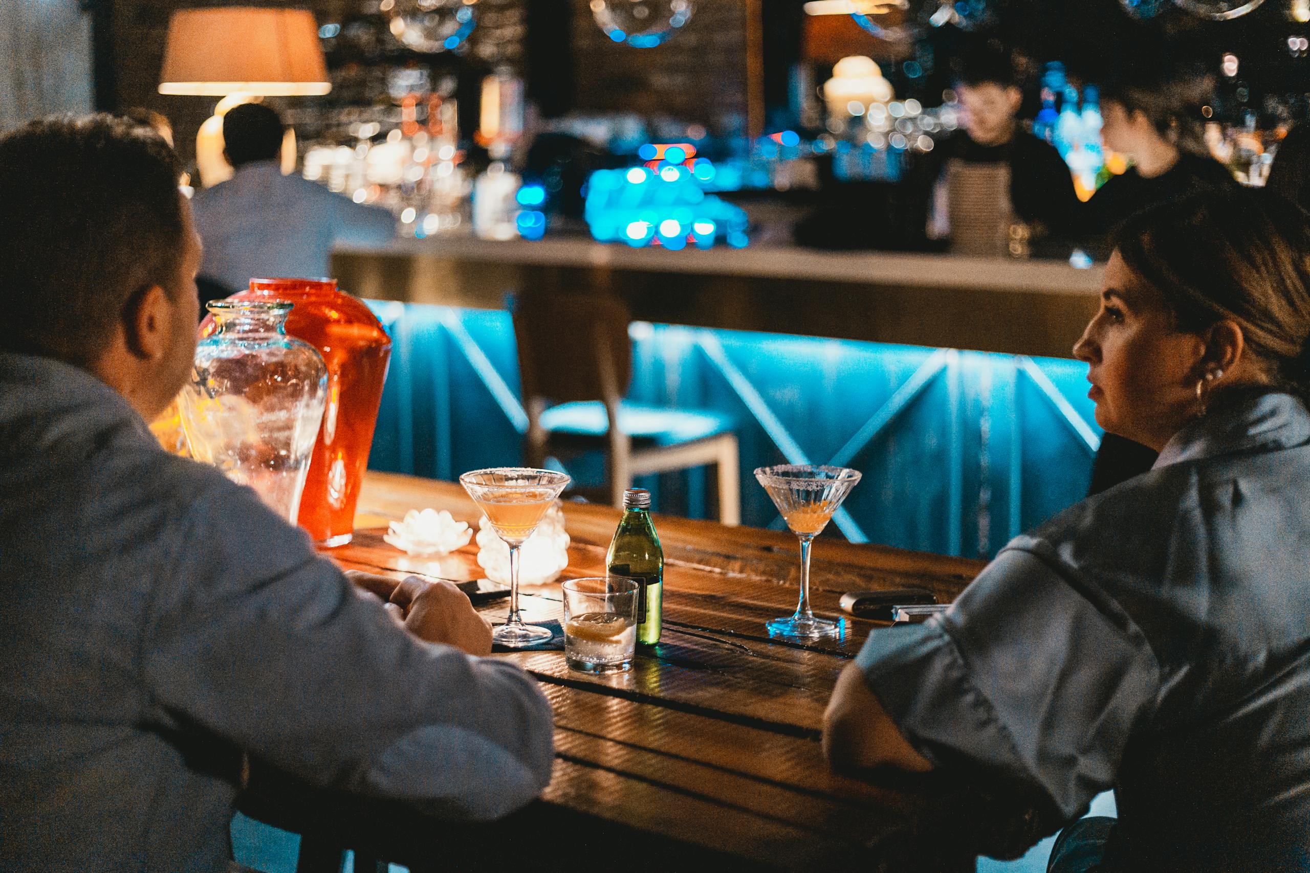 A couple sitting at a bar table with cocktails, creating a cozy evening atmosphere.