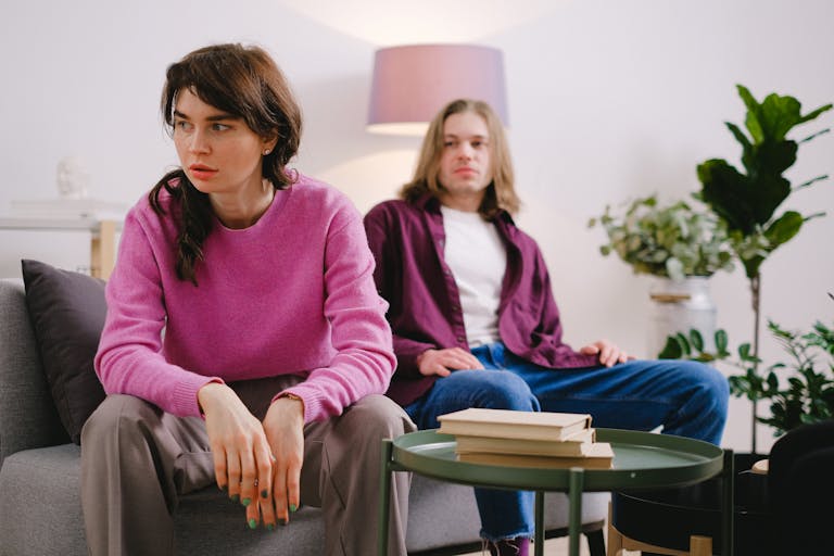 A couple sitting on a sofa with thoughtful expressions, surrounded by home decor.