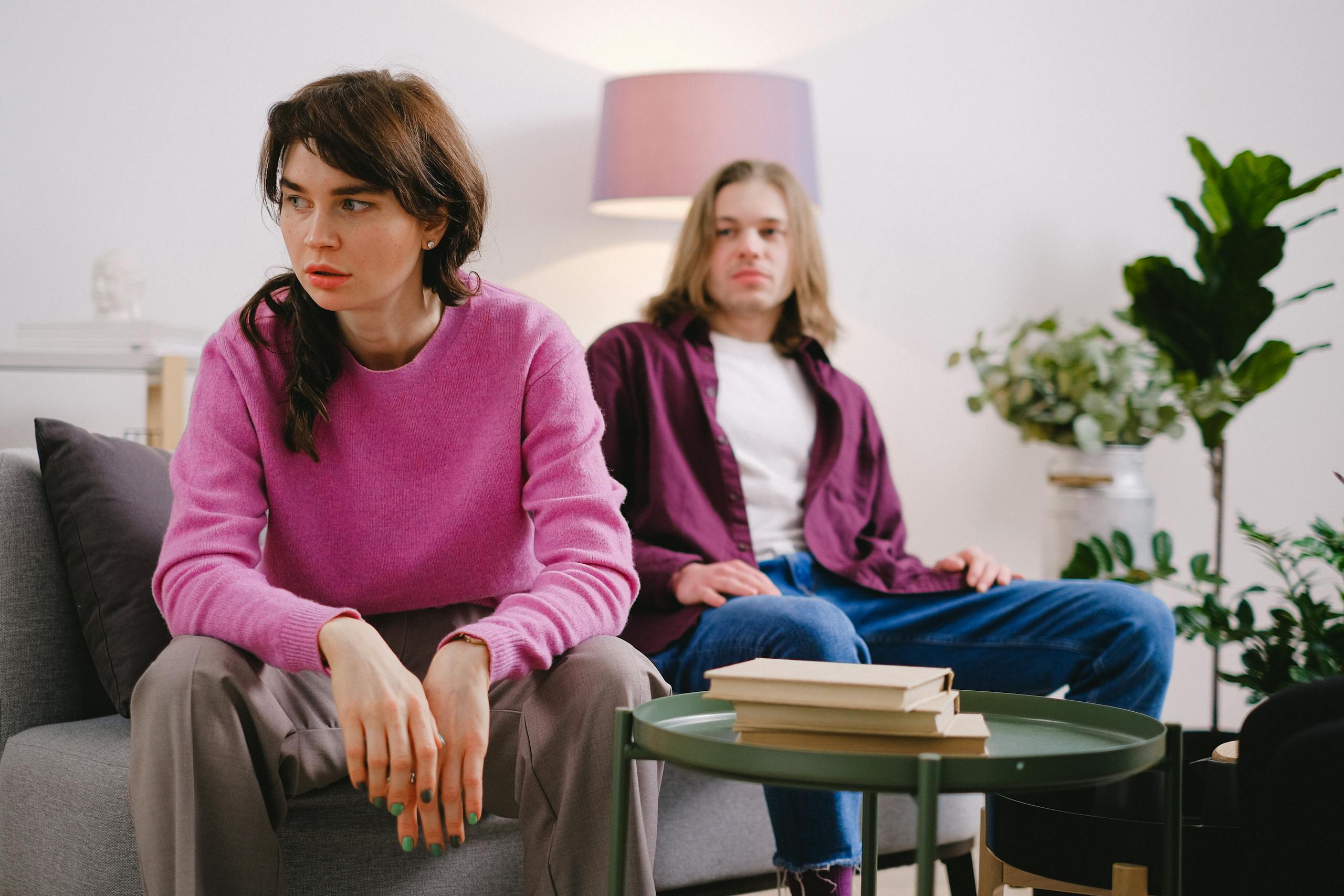 A couple sitting on a sofa with thoughtful expressions, surrounded by home decor.