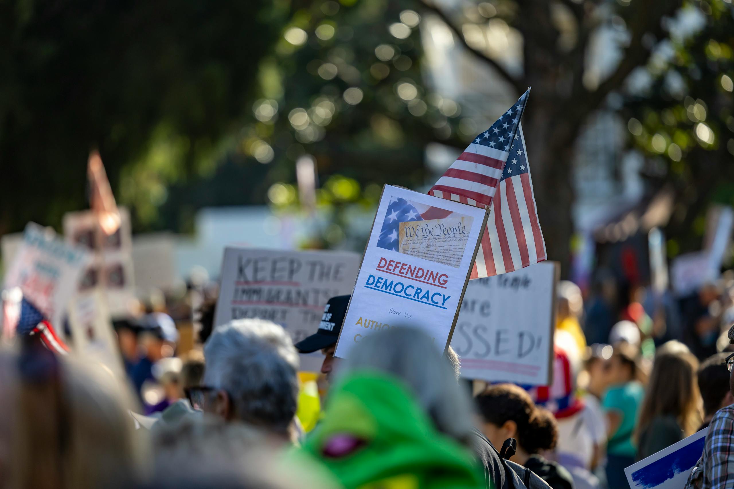 A crowd gathers in Sacramento, California to protest for defending democracy with signs and American flags.