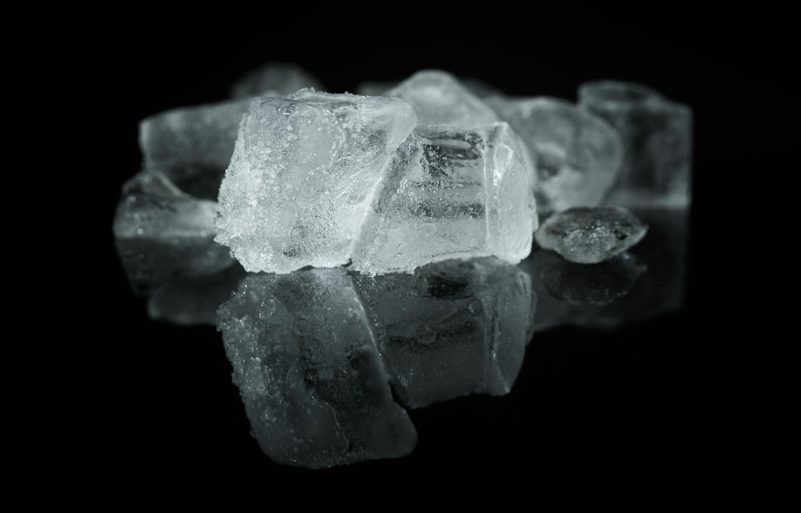 A detailed close-up of ice cubes reflecting on a dark surface, creating a cool ambiance.