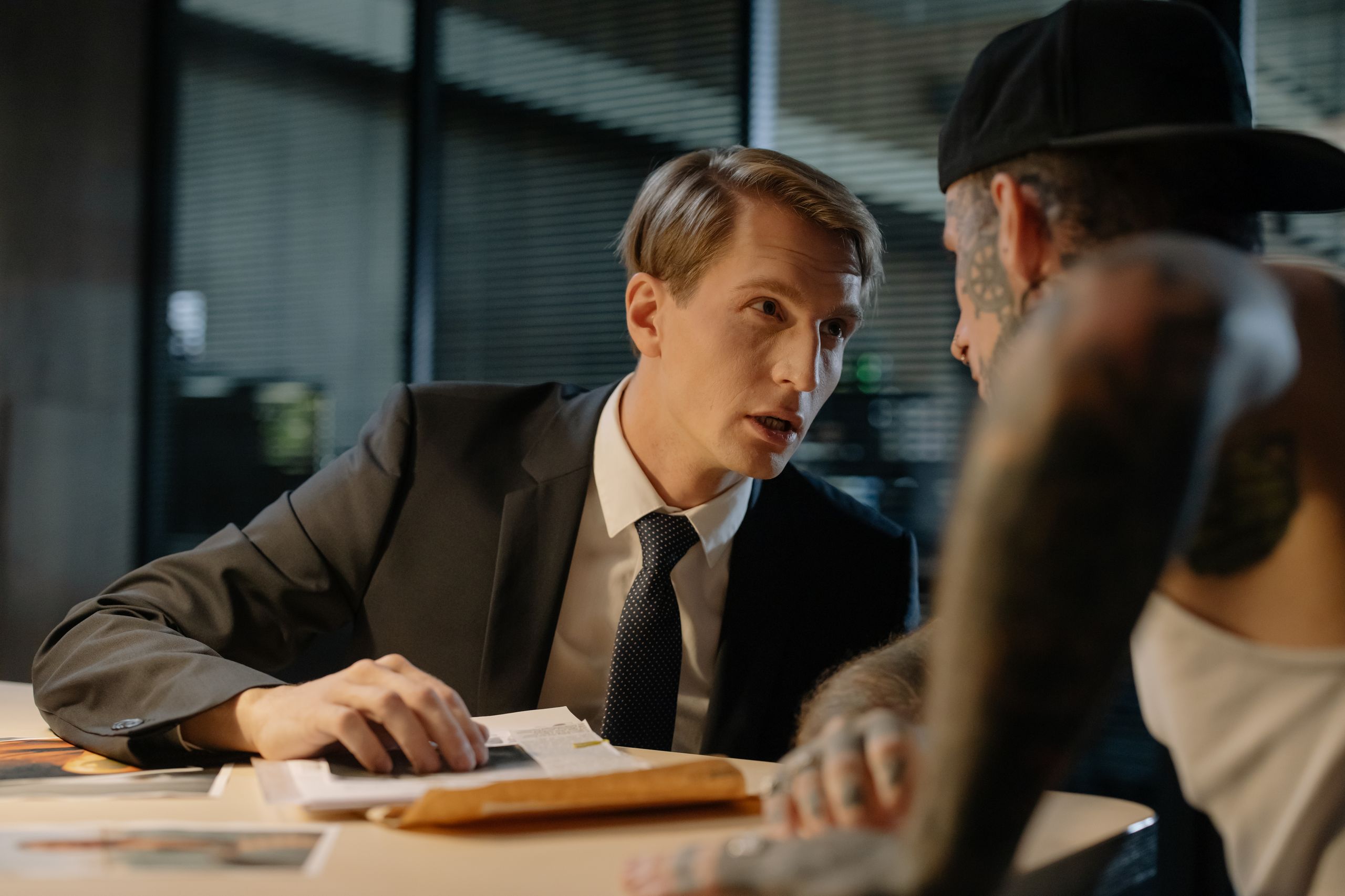 A detective interrogates a tattooed man in an intense indoor office setting.