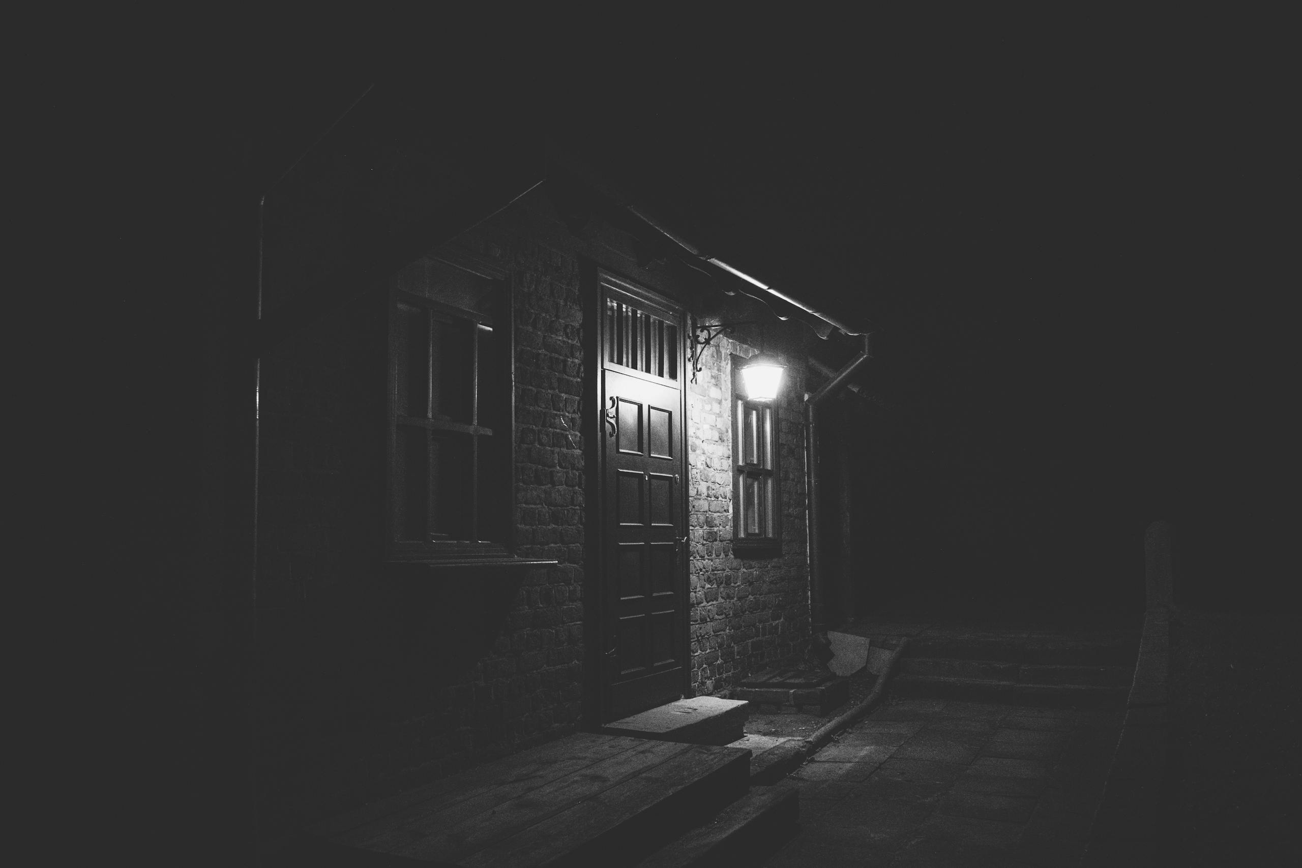 A dramatic night scene of an illuminated brick facade in grayscale, evoking mystery.