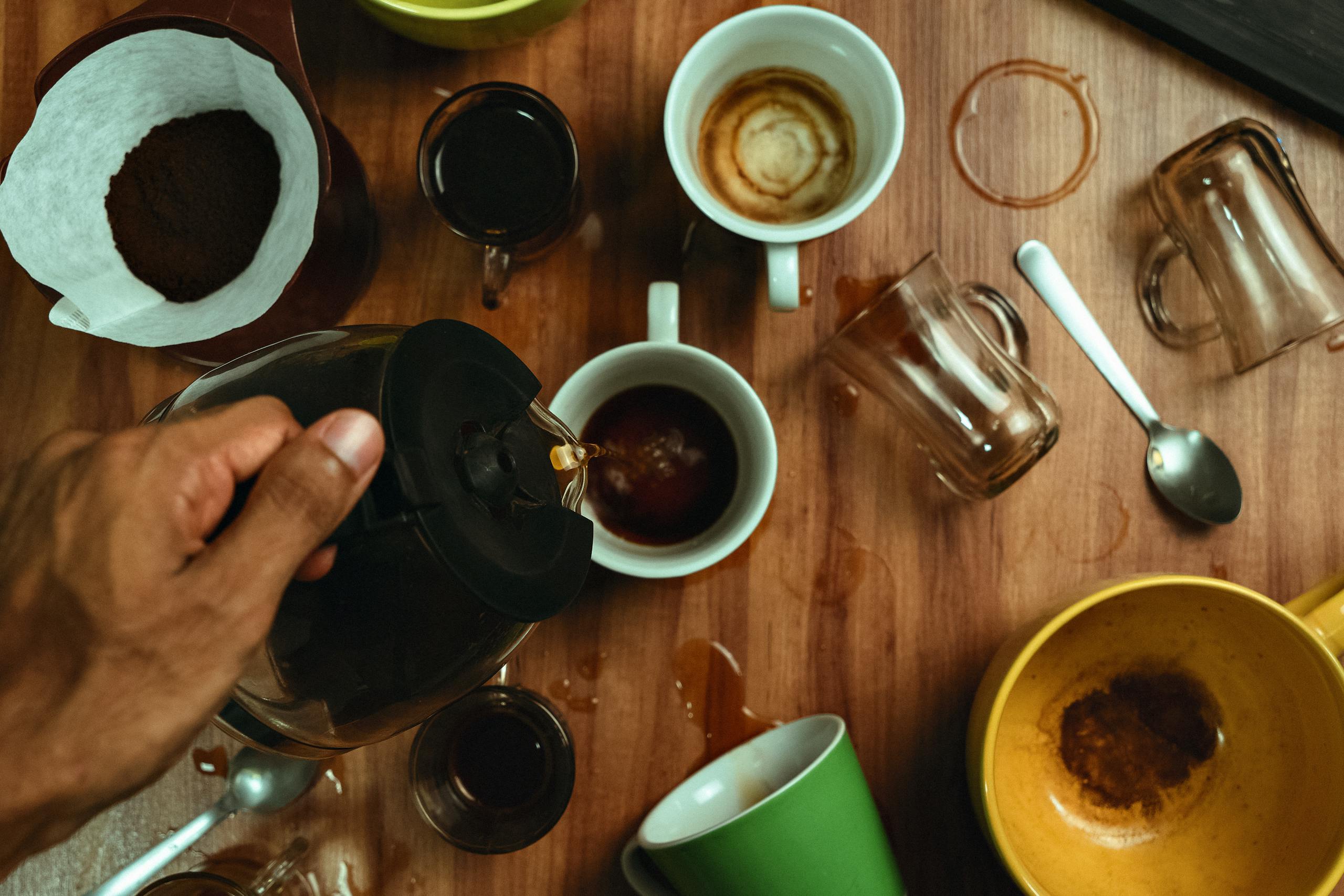 A dynamic scene with coffee being poured into multiple scattered cups on a wooden table, viewed from above.