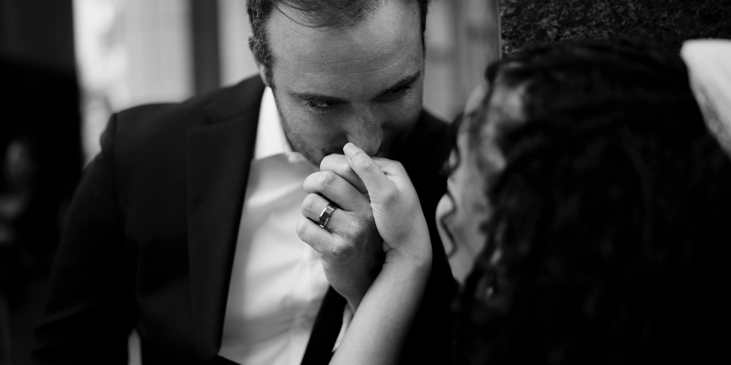 A groom kisses his bride's hand, capturing an intimate wedding moment in black and white.